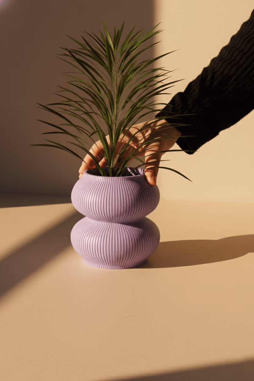 Hand holding a green plant in a textured, double-bulb-shaped purple vase on a beige surface.